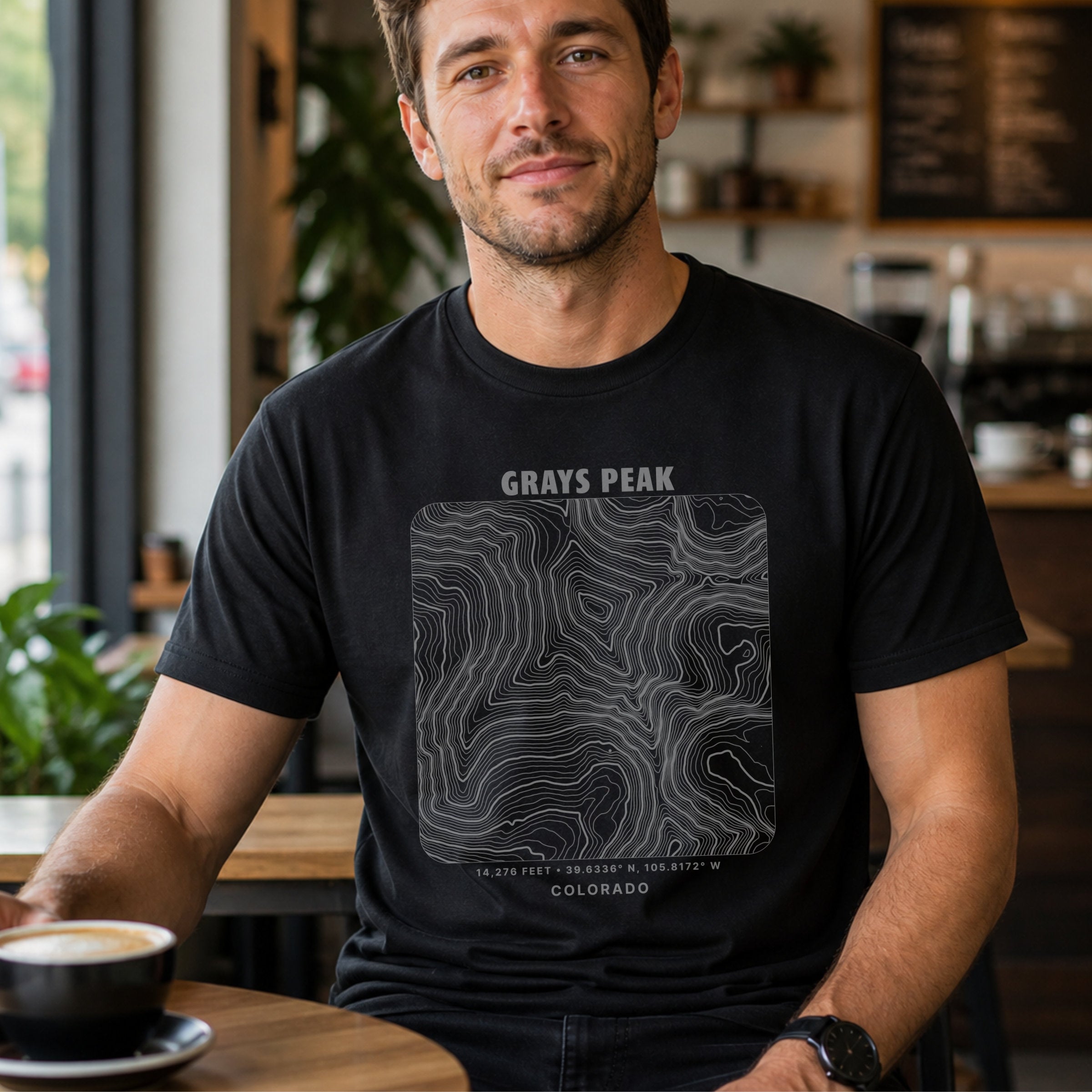 Man seated indoors wearing black t-shirt with square line design